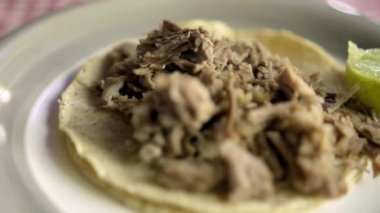 Beef barbacoa taco ve dilimlenmiş limon beyaz ve kırmızı masa örtüsünün üstünde.