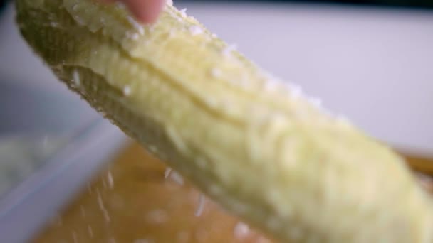 Sprinkling tangan keju pada jagung di atas kayu memotong papan — Stok Video