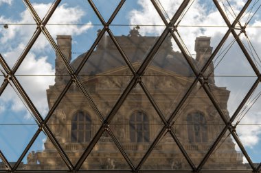 Camdan duvarın arkasından ve bulutlu gökyüzünün altından Louvre Müzesi