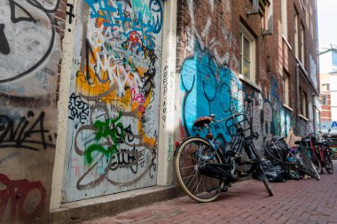 Boş sokağa park edilmiş, duvarlarında grafiti olan bisikletlerin sırası.