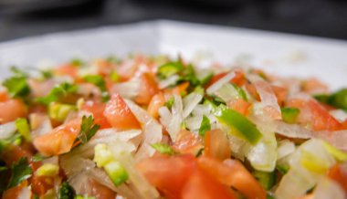 Beyaz tabakta doğranmış domates, soğan ve kırmızı biber.