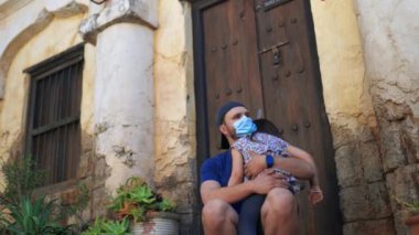 Babası maskeli, uyuyan kızını eski binanın dışına taşıyor.