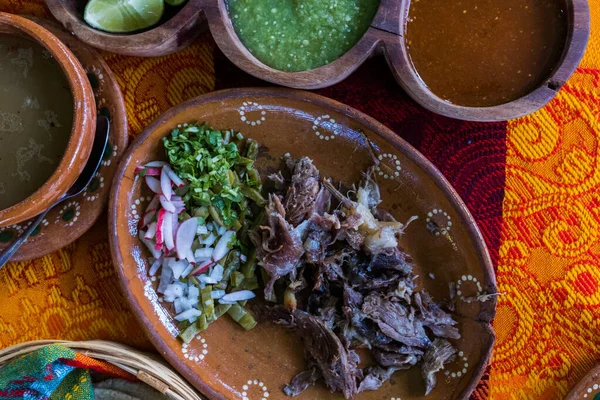Mexican chopped lamb meat, hot sauce, and broth on colorful tablecloth