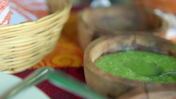 Bowl of hot sauce, palm basket, and roasted meat on colorful tablecloth — Stock Video