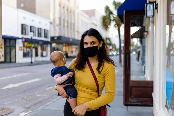 Mãe vestindo máscara facial e segurando seu bebê bonito na rua pacífica — Fotografia de Stock