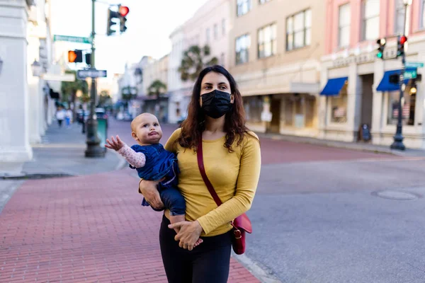 Mãe vestindo máscara facial e segurando seu bebê bonito na rua pacífica — Fotografia de Stock