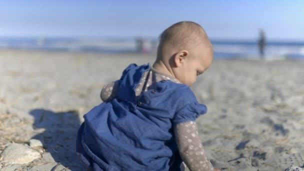 Adoravelmente bebê sentado na areia com azul embaçado mar e céu como fundo — Vídeo de Stock