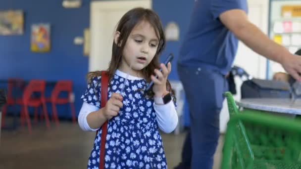 Schattig klein meisje aan de telefoon in een restaurant — Stockvideo