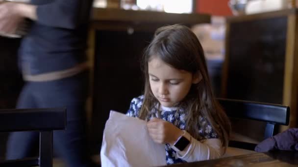 Adorabile bambina a un tavolo che tiene un tovagliolo nel ristorante — Video Stock