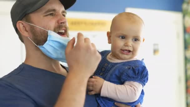 Pai feliz usando uma máscara facial e segurando seu bebê brincalhão bonito — Vídeo de Stock