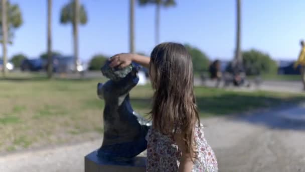 Schattig jong meisje het schoonmaken van het hoofd van een kind standbeeld in een park — Stockvideo