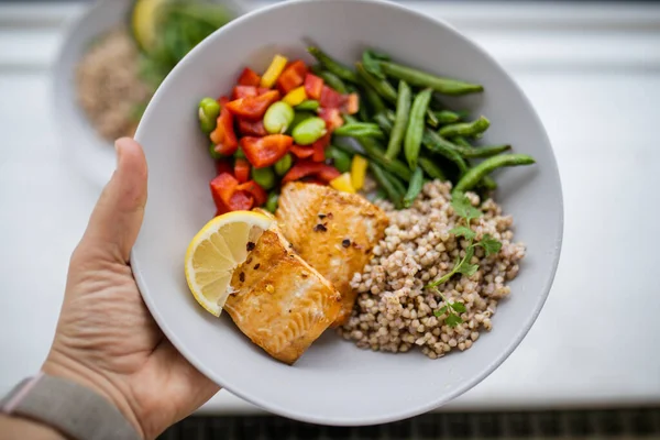 Hand holding salmon and buckwheat dish with green beans