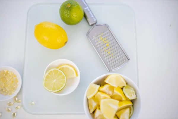 Чашки лайма и ломтики лимона на белом столе рядом с теркой — стоковое фото