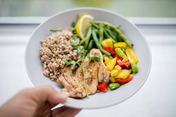 Hand holding a chicken and buckwheat dish with green beans
