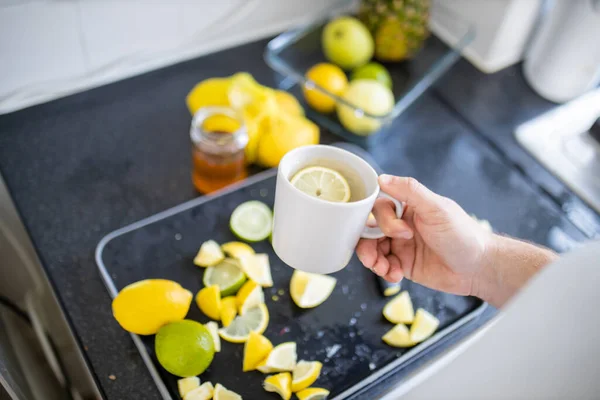 Мужская рука держит чашку лимонного чая над фруктовыми ломтиками — стоковое фото
