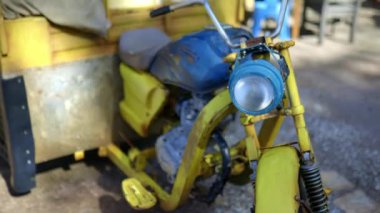 Arka planda bitkiler olan eski mavi ve sarı kargo motosikleti