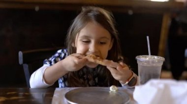 Restoran masasında oturmuş pizza yiyen sevimli küçük kız.