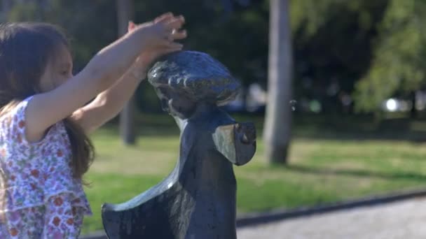 Schattig jong meisje schoonmaken van het standbeeld van een klein kind in een park — Stockvideo