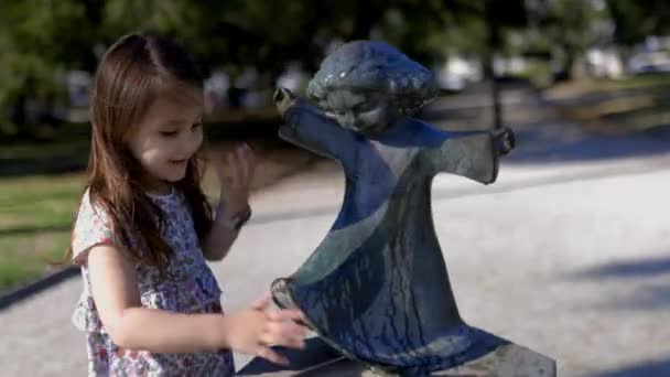 Очаровательная девушка чистит статую маленького ребенка в парке — стоковое видео