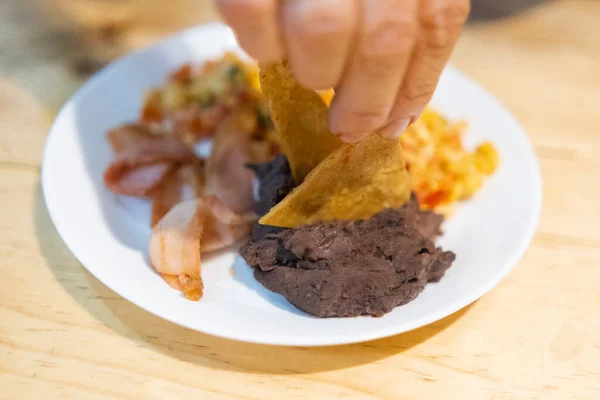 Ruční sběr tortilla chipsů z mexického stylu vejce, slanina, a fazole misky — Stock fotografie