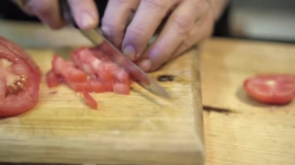 Hands carefully chopping tomato slices above wooden cutting board — Stock Video