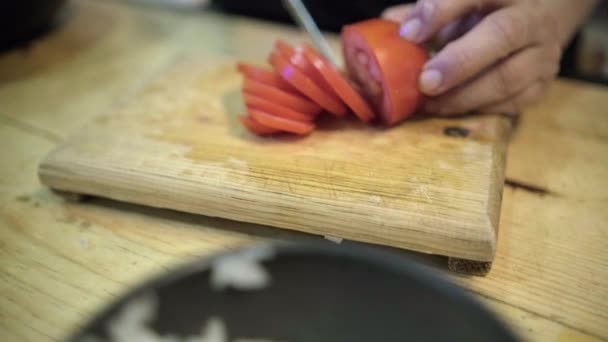 Las manos cortan cuidadosamente un tomate sobre una tabla de cortar de madera — Vídeos de Stock