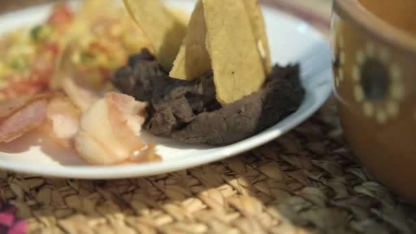 Jaja w stylu meksykańskim, bekon i smażona fasola z frytkami tortilla na białym talerzu — Wideo stockowe