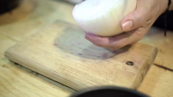 Hands carefully making cuts on half an onion above wooden cutting board — Stock Video