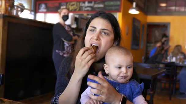 Moeder eten en houden van haar schattige baby in een restaurant — Stockvideo