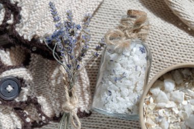 Bej bir tekstil örgü arka planda rahatlatıcı bir banyo için bir şişe deniz tuzu. Küçük bir demet lavantanın yanında.