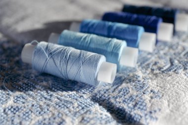 İşlemeli beyaz doğal kumaşa iplik bobini seti. Mavi iplik. Mavinin farklı tonlarında birkaç makara iplik. Seçici odaklanma. İplikli mavi bobinli bir arkaplan