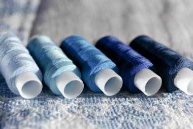 Mavi iplik. İşlemeli beyaz doğal kumaşa iplik bobini seti. Mavinin farklı tonlarında birkaç makara iplik. Seçici odak