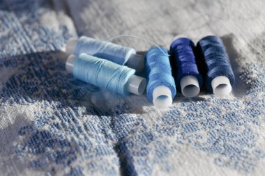 Mavi iplik. Dikiş bobinleri seti. Mavinin farklı tonlarında birkaç makara iplik. Nakışlı beyaz doğal kumaş. Seçici odak