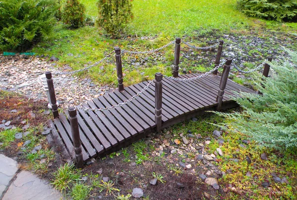 Bahçedeki kahverengi ahşaptan yapılmış küçük ahşap bir köprü. Taşların üzerinde bir köprü.
