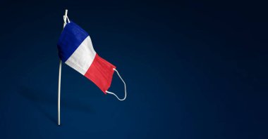 Fransa maskesi koyu mavi arka planda. Direğe tıbbi maske takmış Fransa bayrağı sallıyor. Virüs saldırısı bayrağı. Salgın koronavirüs COVID-19 'a karşı mücadele bayrağı kavramı. Boşluğu kopyala