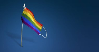 LGBT maskesi koyu mavi arka planda. Direkte tıbbi maskenin üzerine LGBTQ bayrağı sallıyor. Virüs saldırısı bayrağı. Salgın koronavirüs COVID-19 'a karşı mücadele bayrağı kavramı. Boşluğu kopyala
