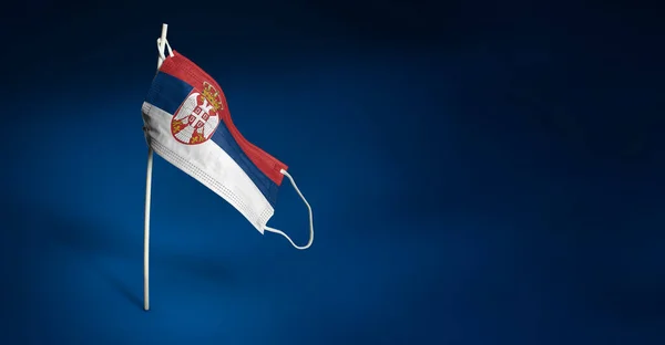 Szerbia maszkot visel sötétkék háttérben. Szerbia zászlaját lobogtatva orvosi maszkra festették a rúdra. A járványos koronavírus elleni küzdelem zászlajának koncepciója COVID-19. Fénymásolási hely — Stock Fotó