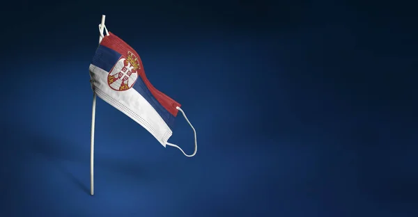 Sırbistan maskesini koyu mavi arka planda tutuyor. Sırığa tıbbi maske takmış Sırbistan bayrağı sallıyor. Salgın koronavirüs COVID-19 'a karşı mücadele bayrağı kavramı. Boşluğu kopyala