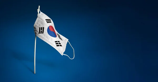 South Korean mask on dark blue background. Waving flag of South Korea painted on medical mask on pole. Concept of The banner of the fight against the epidemic coronavirus COVID-19 — Stock Photo, Image