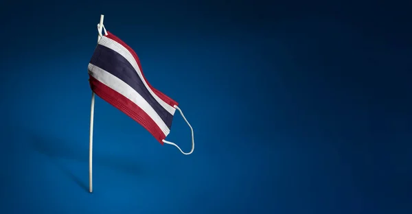 Таиланд маска на темно-синем фоне. Размахивая флагом Таиланда, нарисованный на медицинской маске на шесте. Концепция Знамени борьбы с эпидемией коронавируса COVID-19 — стоковое фото