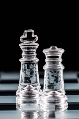 Cam satranç tahtasındaki cam satranç taşları siyah bir arka planda yansıtılıyor..