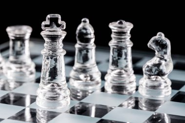 Cam satranç tahtasındaki cam satranç taşları siyah bir arka planda yansıtılıyor..