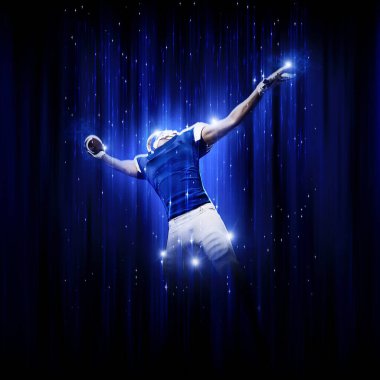 Süper kahraman pozu veren futbolcu siyah arka planda mavi ışıklarla mavi üniforma giyiyor..