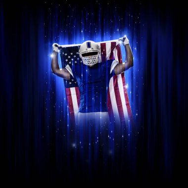 Süper kahraman pozu veren futbolcu siyah arka planda mavi ışıklarla mavi üniforma giyiyor..