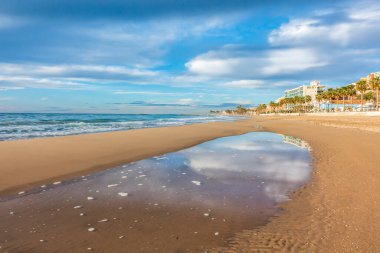 Bulutların yansıması olan Villajoyosa plajı kumdaki su havuzu, Alicante, İspanya.