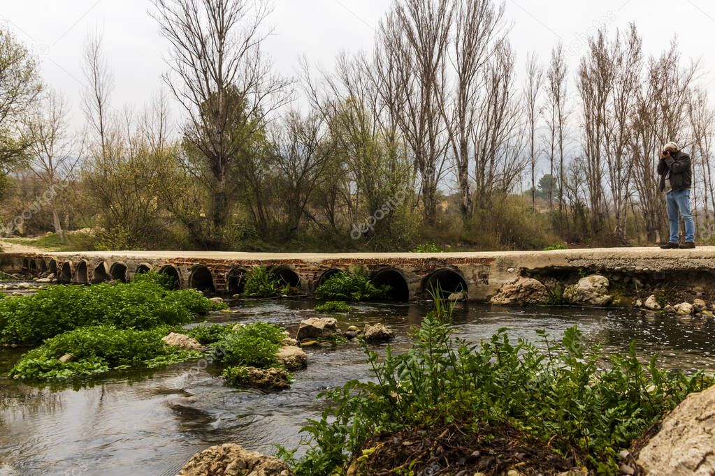 Bridge with small arches over the Serpis river next to the old train track with a photographer in Villalonga, Valencia, Spain.