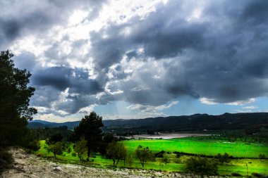 Bir günde yeşil çayır, beyaz ve gri bulutlar ve arkasında dağlar olan güneş ışınları..