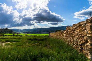 Bir günde yeşil çayır, beyaz ve gri bulutlar ve arkasında dağlar olan güneş ışınları..