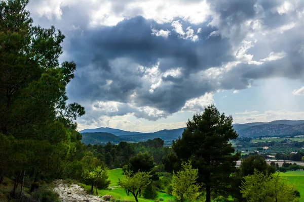 Bir günde yeşil çayır, beyaz ve gri bulutlar ve arkasında dağlar olan güneş ışınları..