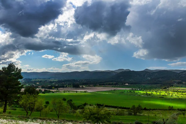 Bir günde yeşil çayır, beyaz ve gri bulutlar ve arkasında dağlar olan güneş ışınları..